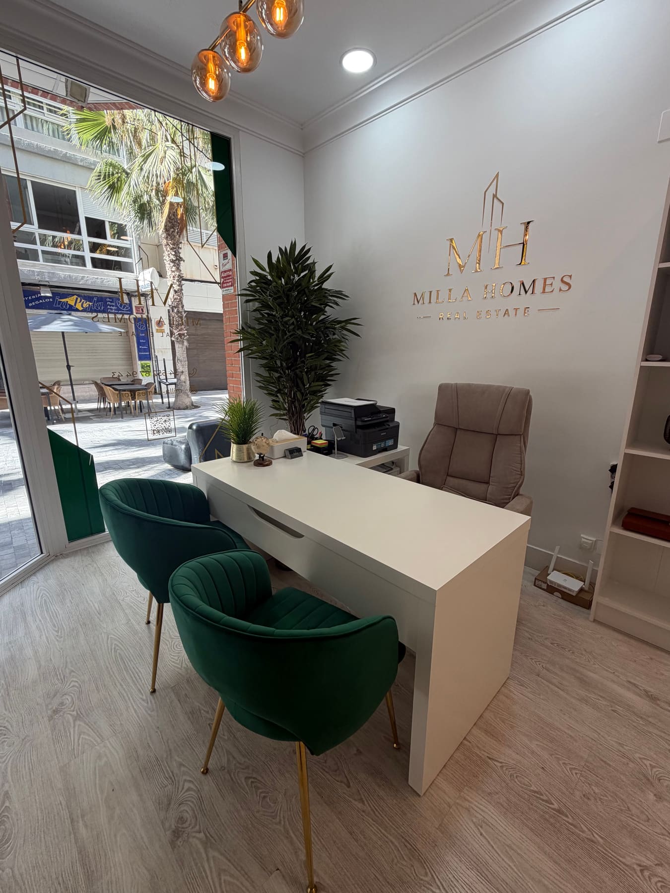 Milla Homes office interior with a white desk, green velvet chairs and the gold Milla Homes logo on the wall